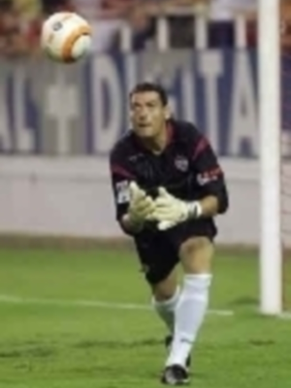 Un jugador de fútbol en acción, con una pelota en el aire y la iluminación del estadio detrás.