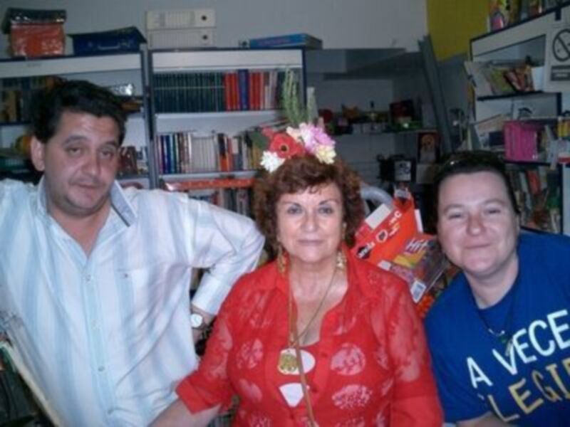 Tres personas sonrientes en una biblioteca con libros y flores.
