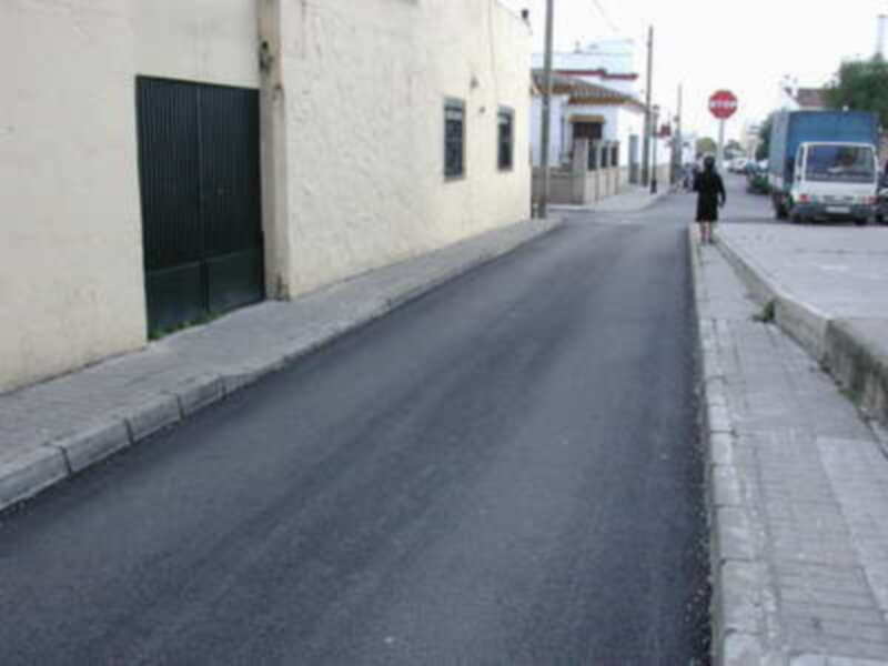 Calle tranquila con edificios blancos y una persona caminando en el borde derecho.