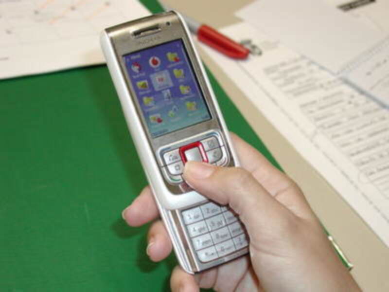 Mano sosteniendo un teléfono móvil Nokia antiguo con teclado numérico y pantalla táctil. Fondo con documentos y bolígrafo rojo.