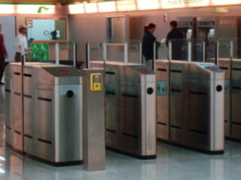 Puertas de control en un aeropuerto, con una señal de salida y gente esperando.