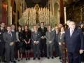 Celebración en una iglesia con altares adornados y personas en trajes formales con medallas.