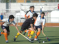 Un partido de hockey en campo abierto con jugadores corriendo y luchando por la pelota.