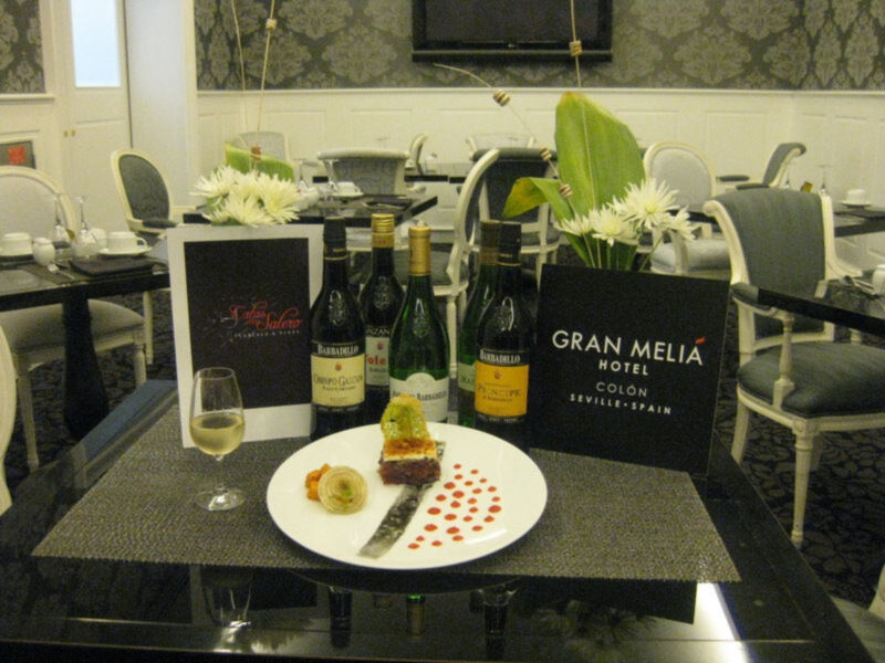 Elegante mesa de té en el Gran Meliá Hotel Colón, Sevilla, con vino, pastel y decoración floral.