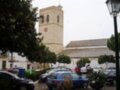 Iglesia de San Bartolomé en Arcos de la Frontera, España, bajo un cielo nublado con árboles y coches alrededor.