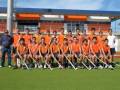 Equipo de hockey sobre césped en uniforme naranja, posando en un campo deportivo con palos de hockey.