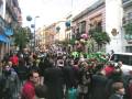 Fiesta en una calle con globos, carros y personas celebrando.