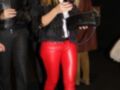Elegante mujer con pantalones de cuero rojo, chaqueta de plumas negra y zapatos de tacón negro, posiblemente en una fiesta o evento formal.