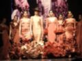 Modelos desfilan en la pasarela de una feria de moda, luciendo vestidos de flamenca coloridos y elaborados.