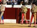 Tres toreros en trajes tradicionales de la tauromaquia, con espadas y capotes, en una plaza de toros.