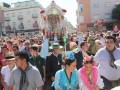 Un grupo de personas en una procesión religiosa, con un altar adornado y flores. La gente está vestida festivamente, algunos con sombreros tradicionales. El ambiente es vibrante y festivo, típico de una celebración religiosa en comunidad.