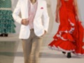 Modelo masculino en traje blanco y pantalones beige, caminando por la pasarela en un desfile de moda flamenca.