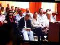 Una audiencia en una sala de tribunal, con personas sentadas y uno leyendo un documento.