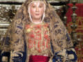 Imagen de una figura religiosa vestida con un manto ornamental y tocado con una corona, posiblemente representando a la Virgen María. La imagen está en un entorno de altar con detalles artísticos y decorativos.