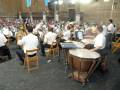 Orquesta sinfónica en un escenario histórico, con músicos tomando notas y ejecutando instrumentos como el timbal y el tuba.