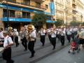 Músicos en una banda de tubas y trompetas tocando al aire libre, con edificios y tiendas en el fondo.