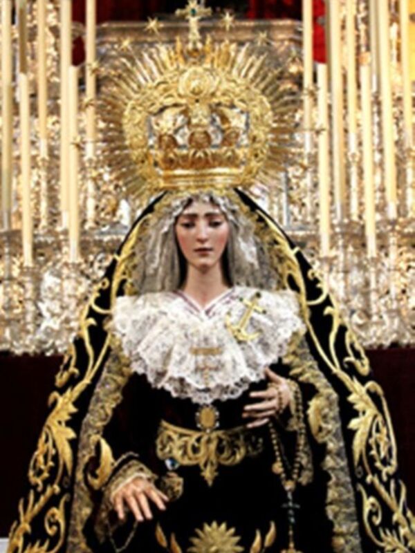 Imagen de una Virgen María con un traje tradicional y una corona dorada, rodeada por velas.