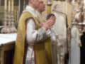 Misa en iglesia, sacerdote con mitra y hábito, altar con velas y coro en segundo plano.