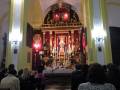 Interior de una iglesia con altares y estatuas, personas sentadas observando la celebración.