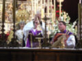 Imagen de una ceremonia religiosa con dos sacerdotes vestidos en trajes coloridos, frente a un altar adornado con velas y flores.