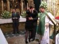 Un momento de reverencia durante una ceremonia religiosa en una iglesia ornamental, con la presencia de personas vestidas formalmente y un sacerdote en vestimenta litúrgica.
