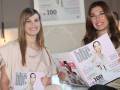 Dos mujeres sonríen mostrando revistas con portadas similares.