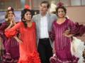 Una escena festiva con cuatro personas vestidas en trajes flamencos coloridos, posiblemente en una competencia o desfile cultural. La imagen muestra a dos mujeres con vestidos rojos y una mujer en un vestido rosa, junto a un hombre en traje gris. La escena parece ser parte de una celebración o evento cultural, con un fondo que sugiere un ambiente festivo.