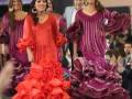 Modelos desfilando en un evento de moda, destacándose por sus vestidos tradicionales flamencos de colores vibrantes.