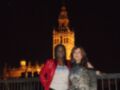 Dos personas posan frente a la Giralda de Sevilla, iluminada por las luces nocturnas.