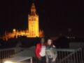 Dos personas posan frente a la Giralda de Sevilla iluminada en la noche.