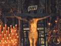 Imagen de un crucificado en una iglesia, rodeado por velas encendidas y decoraciones navideñas.