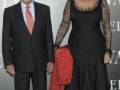 Dos personas posan en una alfombra roja. La persona de la izquierda lleva un traje negro y corbata rosa, mientras que la otra lleva una vestido largo negro con detalles de encaje. La imagen parece ser de un evento formal, posiblemente una gala o premiación.