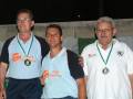 Tres personas sonrientes con medallas en un podio nocturno.
