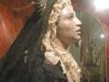 Una figura vestida con una capa negra y un velo largo, posiblemente representando a la Virgen María, con detalles dorados en su vestimenta.