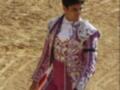 Un torero en traje tradicional de color rosa y blanco, con un fondo de arena.