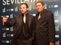 Dos hombres en trajes negros posan frente a un fondo con el logo del Festival de Cine de Sevilla.