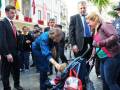 Una imagen de una mujer mayor bendiciendo a un bebé en un carrito, rodeada por personas con trajes formales y uniformes policiales.