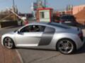 Elegant silver Audi R8 sports car parked on a street corner, surrounded by urban scenery.