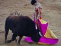 Un torero en el centro de la plaza de toros, con un toro en el fondo, durante una corrida de toros.