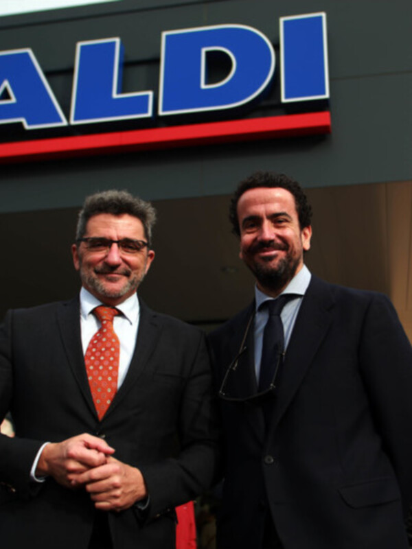 Dos hombres en trajes de negocios frente a una tienda Aldi.