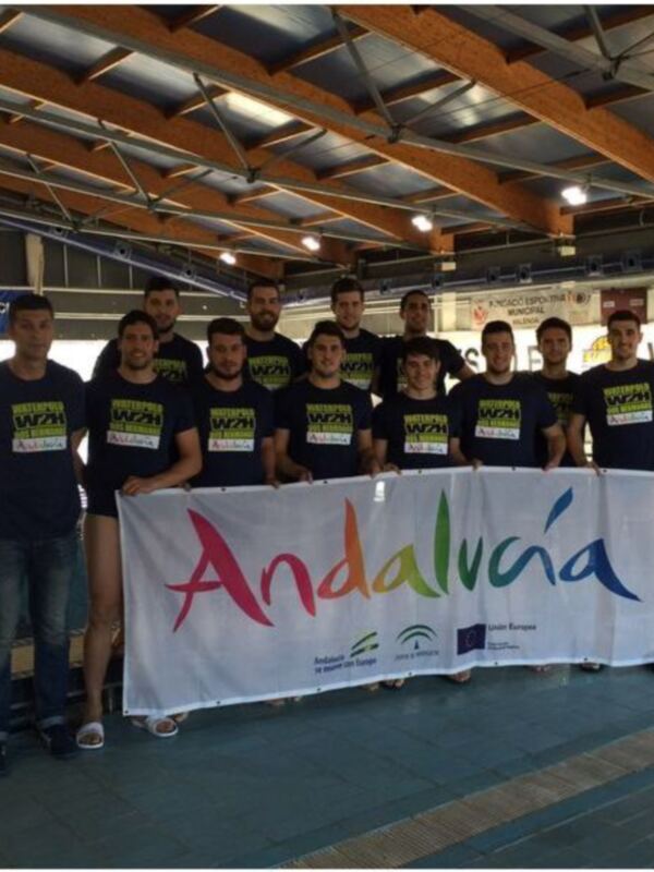 Equipo de natación celebrando con una bandera que dice "Andalucía" en un estadio de natación.