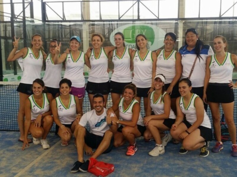 Equipo femenino de padel posando en la cancha, con uniformes blancos y verdes.