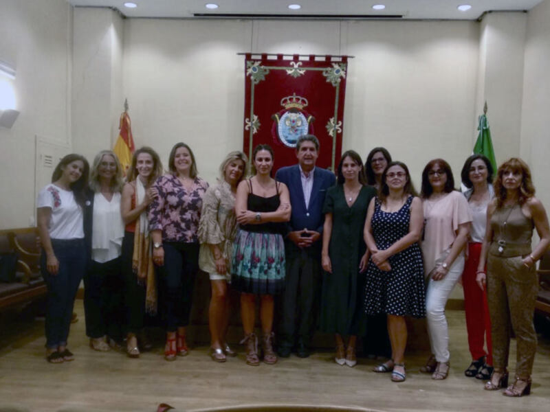 Grupal de personas posando frente a una bandera y un escudo, en un entorno interior.