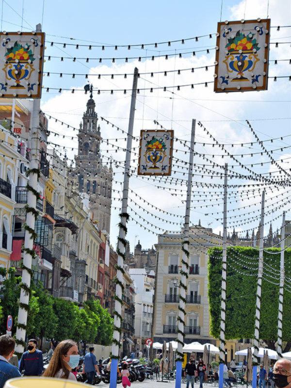 Calle decorada con luces y azulejos típicos de Sevilla, con la Giralda al fondo.