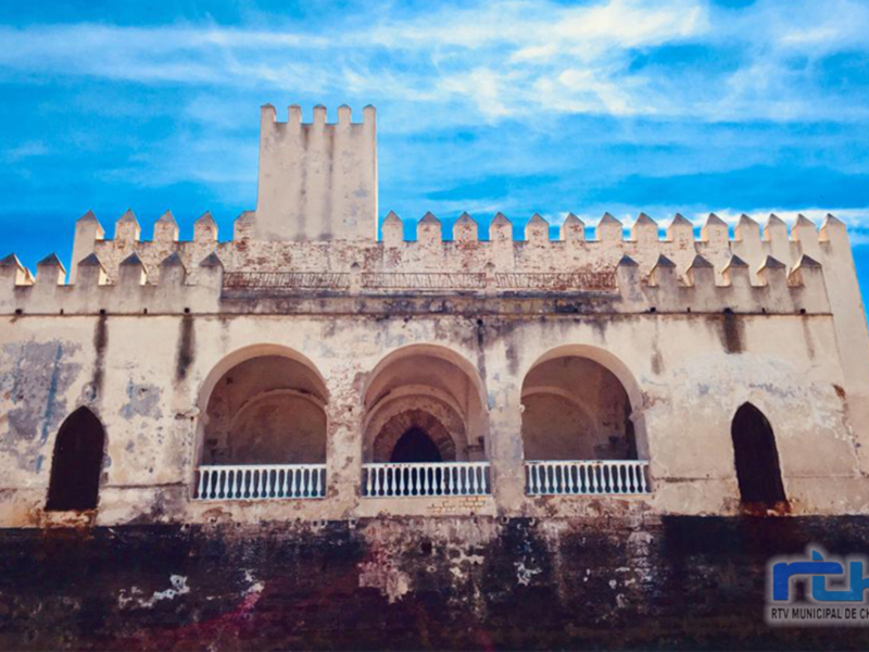 Fachada antigua de un edificio histórico con arcos y torreón, bajo un cielo azul.