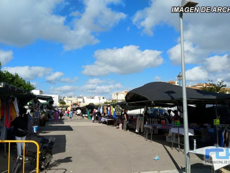 Mercado de abastos con tiendas y personas caminando bajo un cielo azul con nubes.