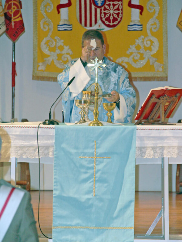 Elegante altar con mantel azul y cruz dorada, acompañado por un libro abierto y una bandera con símbolos religiosos en el fondo.