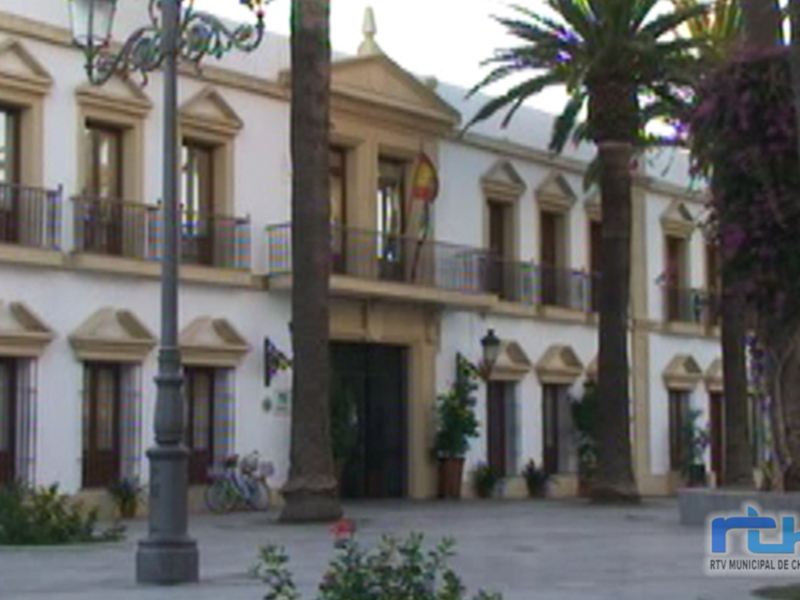 Fachada de un edificio histórico con balcones y palmeras, en un entorno urbano.