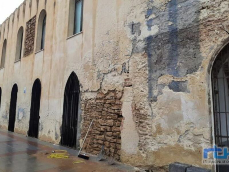 Fachada de un edificio histórico con muros antiguos y una puerta arqueada. La imagen muestra detalles de la arquitectura medieval, con un cielo nublado.
