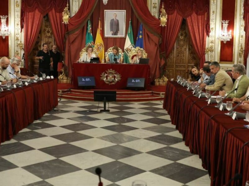 Reunión formal en un salón de conferencias con mesas largas, sillas y una bandera en el fondo.